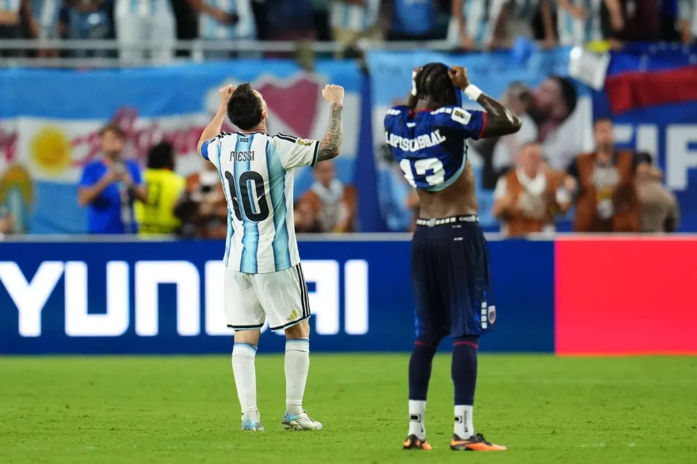 Messi celebra mientras un jugador de Cabo Verde lamenta la derrota en el partido donde Argentina eliminó a Cabo Verde. Messi celebra mientras un jugador de Cabo Verde lamenta la derrota en el partido donde Argentina eliminó a Cabo Verde.